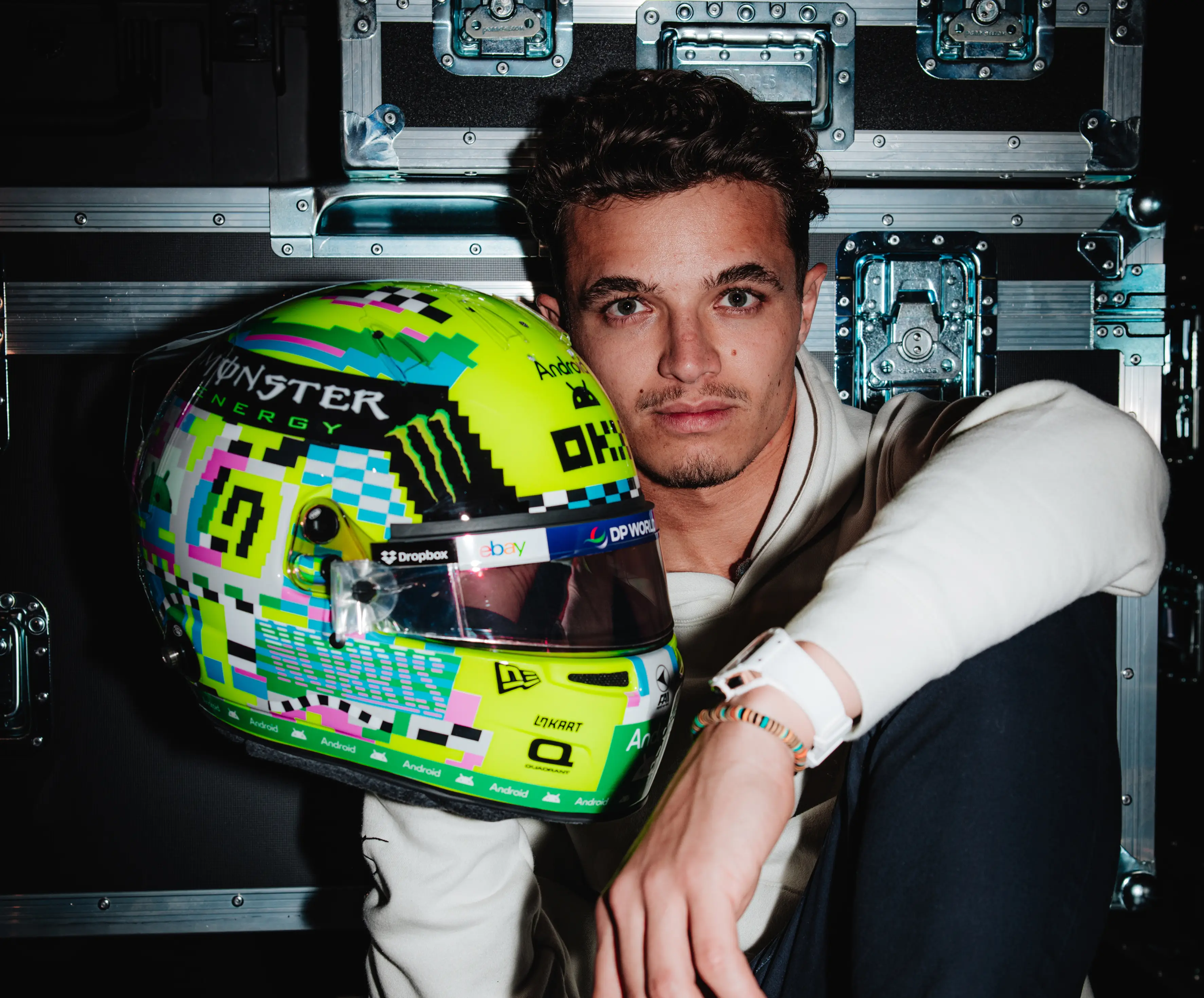 Lando Norris holding up a helmet with flight cases in the background